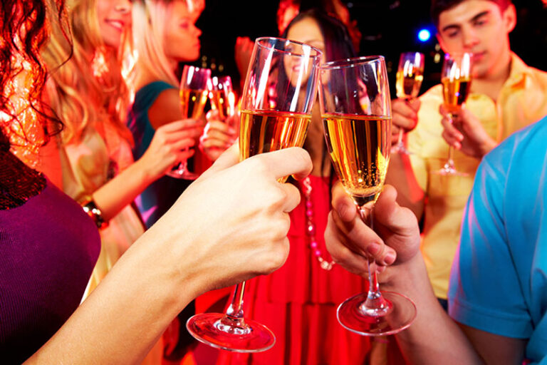 A group of people holding and clinking champagne glasses while celebrating at a lively party, with colorful lights in the background.