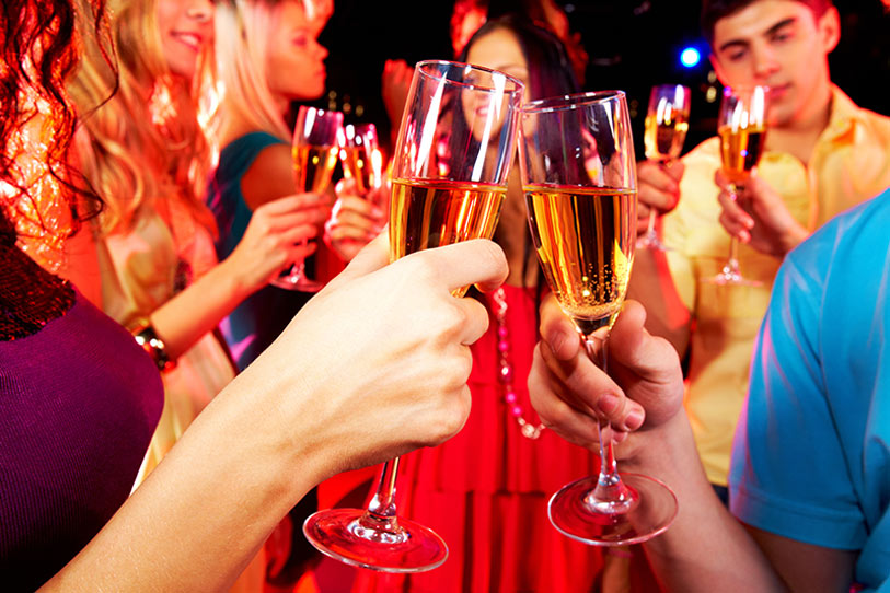 A group of people holding and clinking champagne glasses while celebrating at a lively party, with colorful lights in the background.